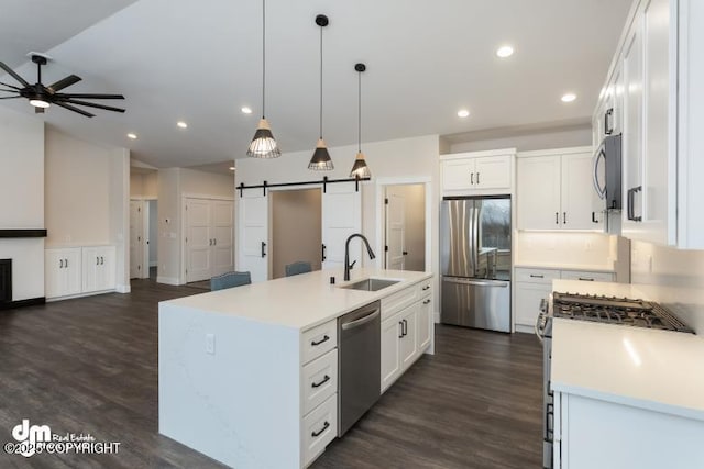 kitchen with pendant lighting, white cabinetry, stainless steel appliances, an island with sink, and a barn door