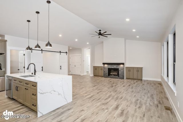 kitchen featuring pendant lighting, lofted ceiling, a kitchen island with sink, light stone counters, and a barn door