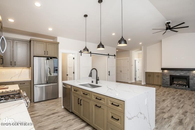 kitchen with sink, stainless steel appliances, light stone countertops, decorative light fixtures, and a barn door