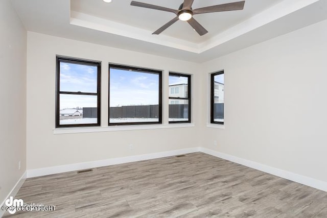 unfurnished room featuring a raised ceiling, ceiling fan, and light hardwood / wood-style flooring