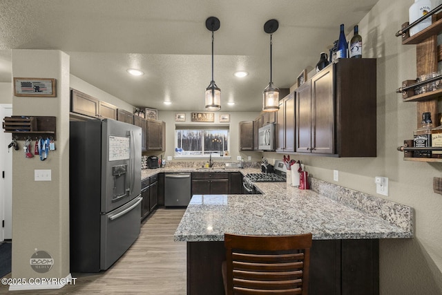 kitchen with sink, hanging light fixtures, a textured ceiling, appliances with stainless steel finishes, and kitchen peninsula