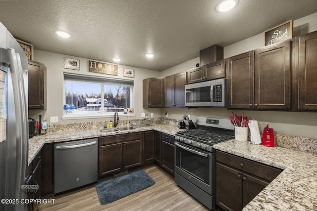 kitchen featuring appliances with stainless steel finishes, sink, light wood-type flooring, dark brown cabinetry, and a textured ceiling