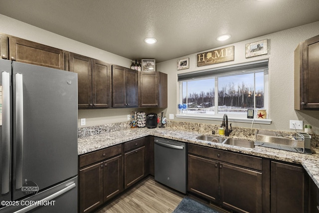 kitchen featuring appliances with stainless steel finishes, sink, dark brown cabinetry, light hardwood / wood-style floors, and light stone countertops