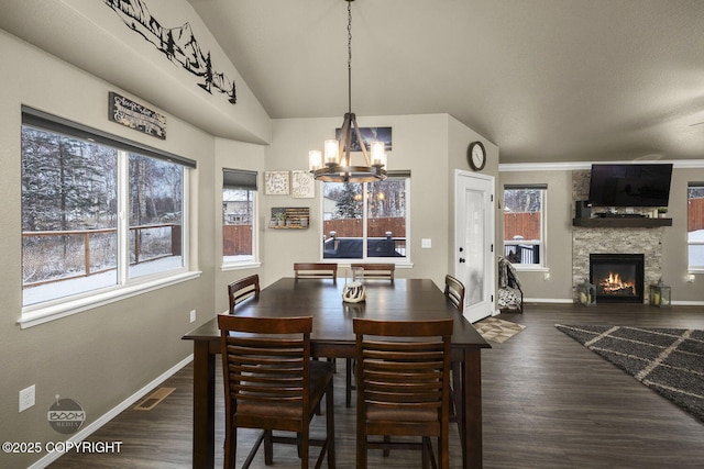 dining space with dark hardwood / wood-style flooring, a stone fireplace, lofted ceiling, and a chandelier