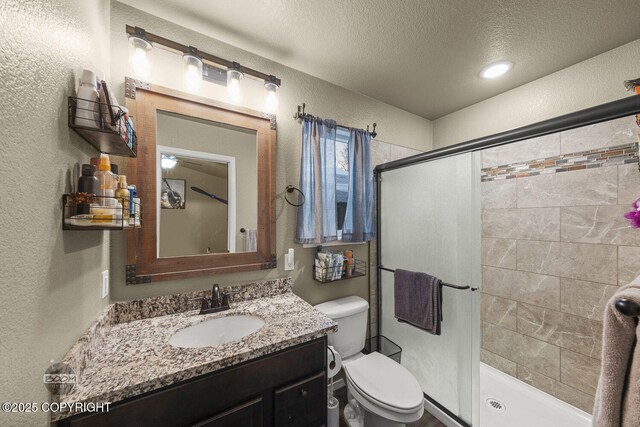 bathroom with vanity, a shower with door, toilet, and a textured ceiling