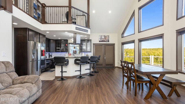 kitchen featuring stainless steel fridge with ice dispenser, island range hood, a kitchen breakfast bar, and a high ceiling