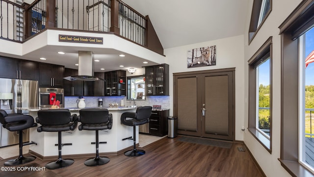 kitchen featuring a breakfast bar area, island range hood, appliances with stainless steel finishes, a kitchen island, and a high ceiling