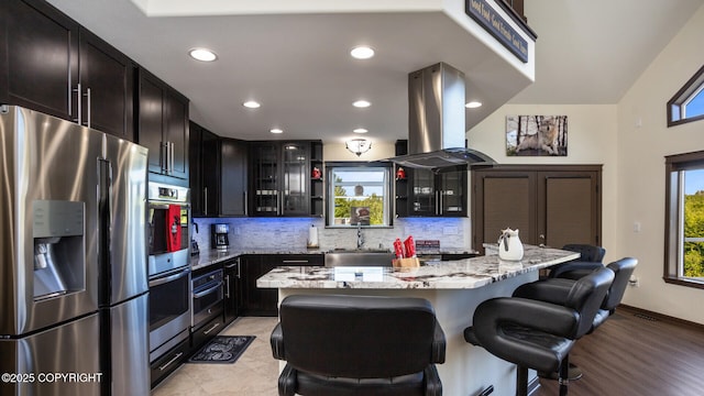 kitchen with a breakfast bar, island exhaust hood, a center island, light stone counters, and stainless steel appliances