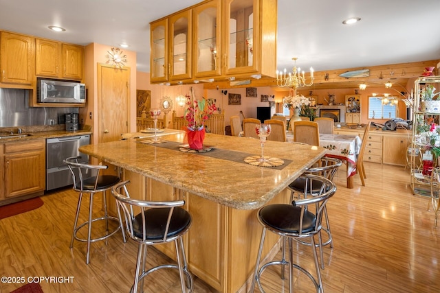 kitchen featuring stainless steel appliances, light wood-type flooring, a breakfast bar area, and a notable chandelier