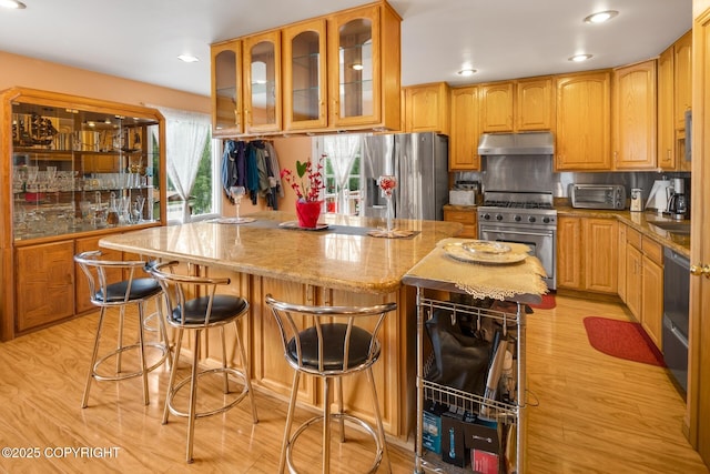 kitchen with appliances with stainless steel finishes, a center island, light stone counters, and light hardwood / wood-style floors