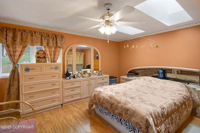 bedroom featuring ceiling fan, a skylight, ornamental molding, light hardwood / wood-style floors, and a textured ceiling