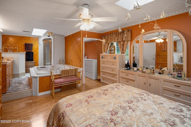 bedroom featuring ceiling fan, wooden walls, a skylight, and a textured ceiling