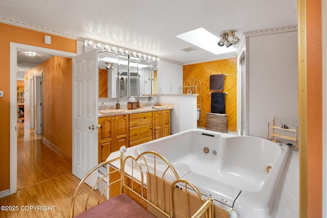 bathroom with a skylight, a textured ceiling, ornamental molding, a bathing tub, and hardwood / wood-style floors