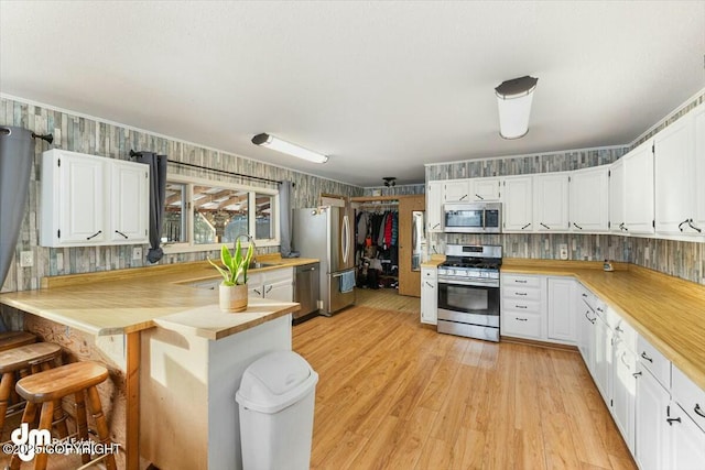 kitchen with stainless steel appliances, white cabinetry, and light hardwood / wood-style flooring