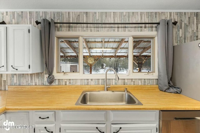 kitchen featuring white cabinetry, sink, stainless steel dishwasher, and crown molding