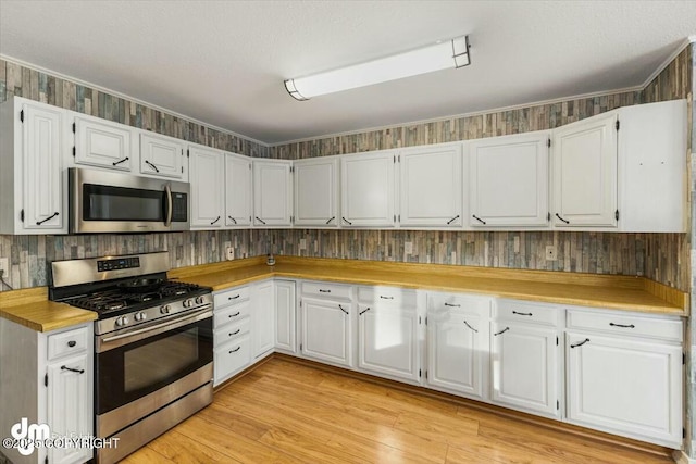 kitchen featuring stainless steel appliances, a textured ceiling, white cabinets, and light wood-type flooring