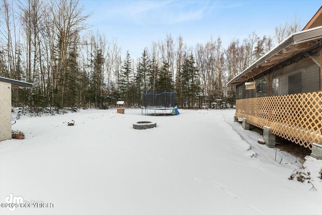 yard layered in snow featuring a trampoline and a fire pit