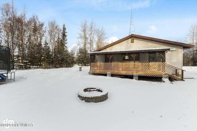 snow covered rear of property featuring a trampoline and an outdoor fire pit