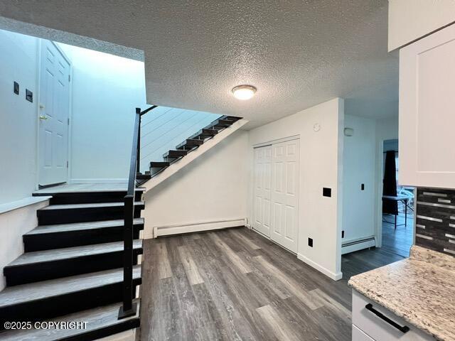 stairway with hardwood / wood-style floors, a textured ceiling, and baseboard heating