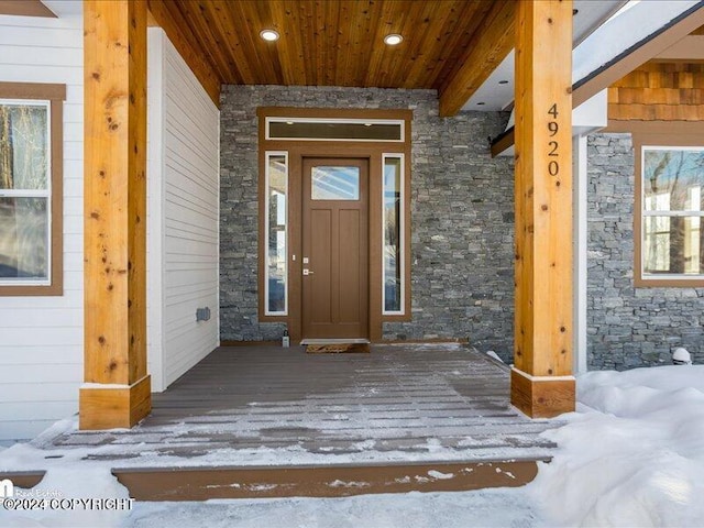 snow covered property entrance featuring stone siding and a porch