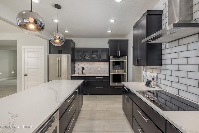 kitchen featuring pendant lighting, sink, backsplash, stainless steel appliances, and wall chimney exhaust hood