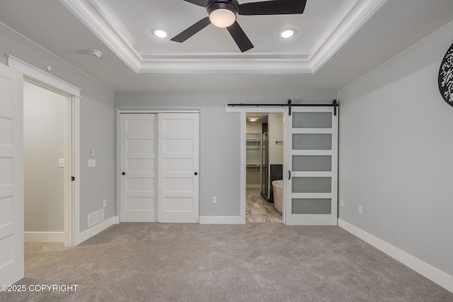 unfurnished bedroom featuring ornamental molding, a barn door, a raised ceiling, and light carpet