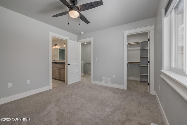 unfurnished bedroom with ceiling fan, connected bathroom, light carpet, a walk in closet, and a closet