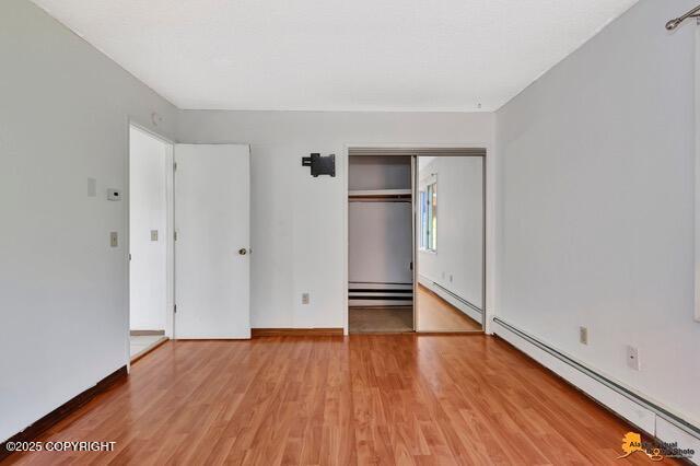 7750 Boundary Ave # A3, Anchorage, AK 99504 - unfurnished bedroom featuring baseboard heating, light wood-style flooring, a closet, and a baseboard radiator