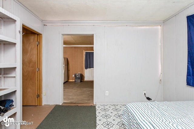 bedroom with ornamental molding, wood walls, and white refrigerator