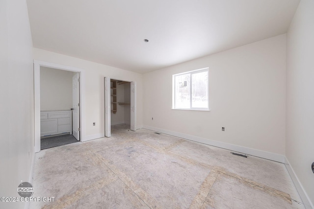 unfurnished bedroom featuring connected bathroom and a spacious closet