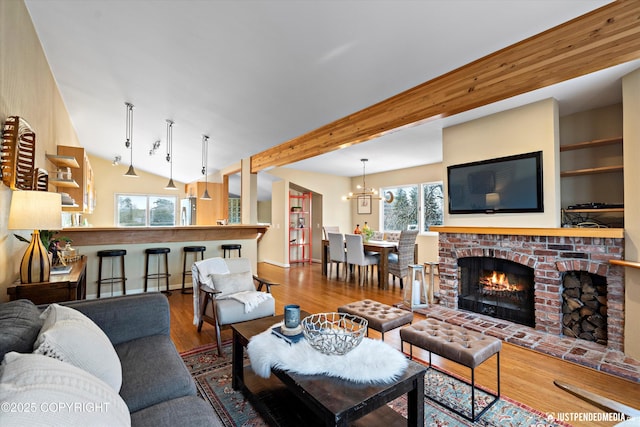 living room with hardwood / wood-style flooring, a fireplace, a chandelier, and vaulted ceiling with beams