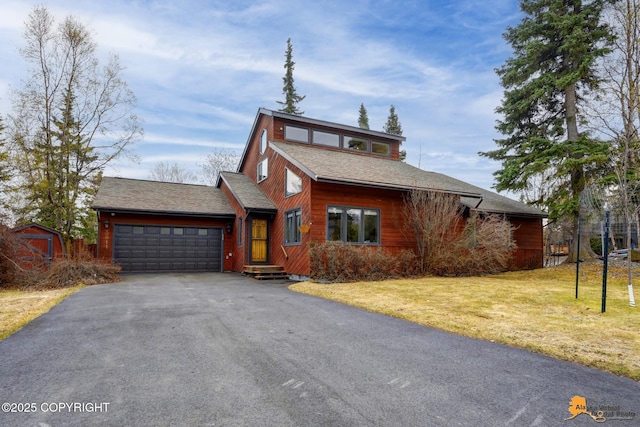 view of front of property with a front yard, a storage unit, a shingled roof, an attached garage, and driveway