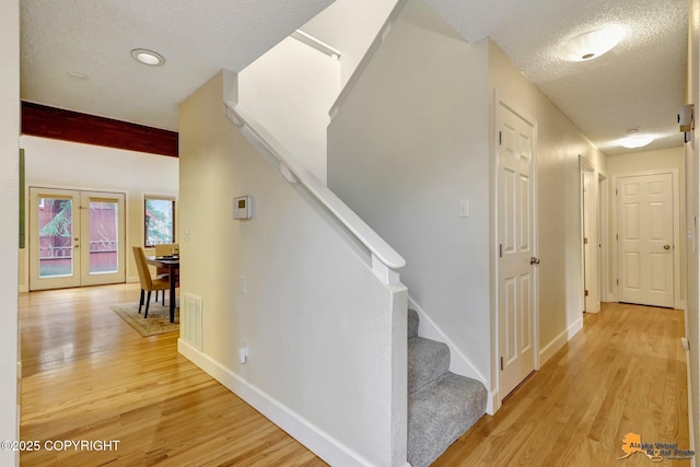 stairway featuring french doors, a textured ceiling, baseboards, and wood finished floors