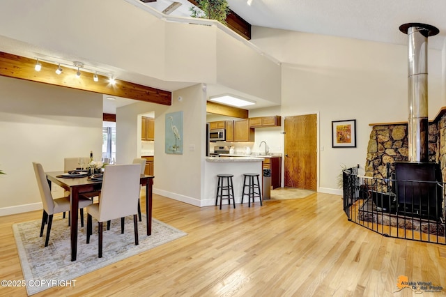 dining area with beamed ceiling, baseboards, a wood stove, and light wood-type flooring