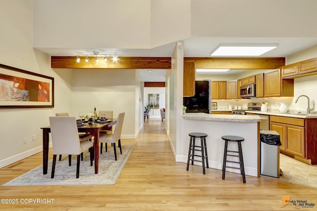 kitchen featuring appliances with stainless steel finishes, a breakfast bar, a sink, light wood-style floors, and light countertops