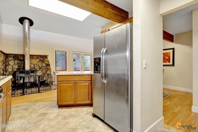 kitchen with a wood stove, stainless steel fridge with ice dispenser, light countertops, brown cabinetry, and light wood-type flooring