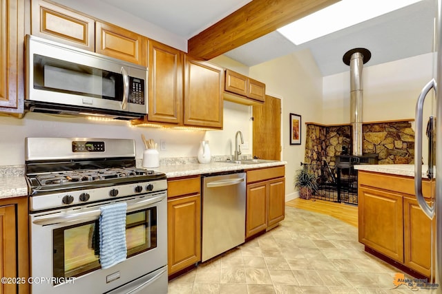 kitchen with brown cabinetry, appliances with stainless steel finishes, a wood stove, a sink, and light countertops