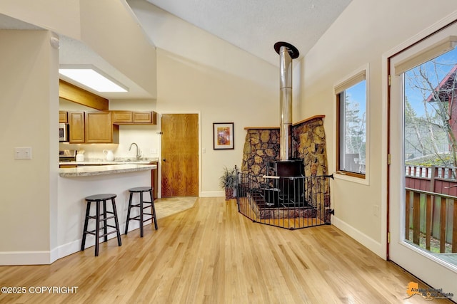 living room with baseboards, a wood stove, light wood finished floors, and high vaulted ceiling