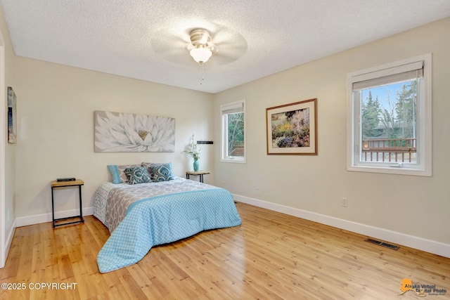 bedroom with visible vents, a textured ceiling, baseboards, and wood finished floors