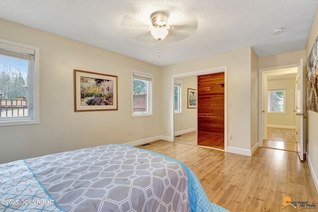 bedroom with light wood-style floors, a textured ceiling, visible vents, and multiple windows