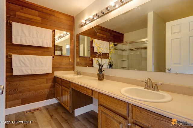 bathroom with visible vents, a sink, wooden walls, and a shower stall