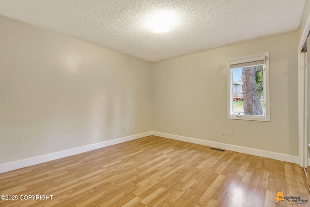 empty room with visible vents, a textured ceiling, light wood-style floors, and baseboards