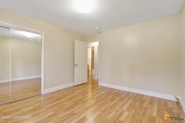 unfurnished bedroom featuring a closet, a textured ceiling, baseboards, and light wood-type flooring