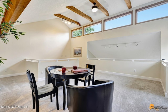 carpeted dining room with ceiling fan, beam ceiling, rail lighting, high vaulted ceiling, and baseboards