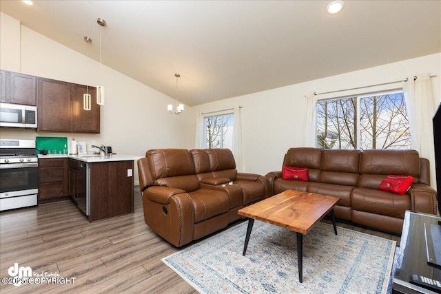 living room with a notable chandelier, high vaulted ceiling, sink, and light wood-type flooring