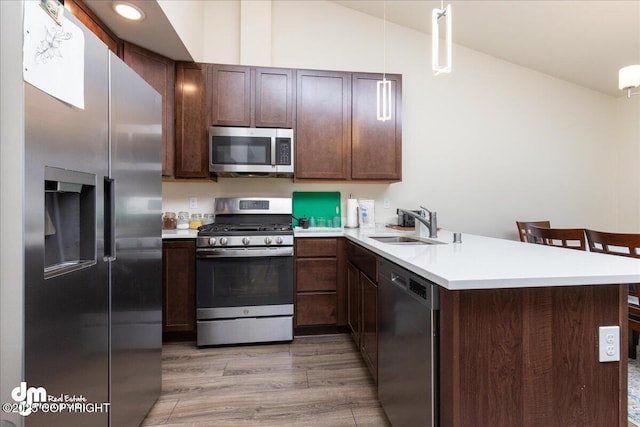 kitchen featuring lofted ceiling, sink, appliances with stainless steel finishes, hanging light fixtures, and kitchen peninsula