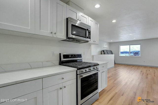 kitchen featuring stainless steel appliances, white cabinetry, light stone countertops, and light hardwood / wood-style floors