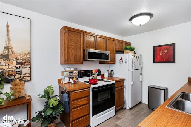 kitchen with sink, light wood-type flooring, white fridge, and electric range