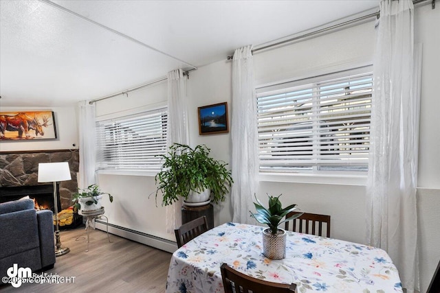 dining space with a baseboard heating unit, hardwood / wood-style floors, and a fireplace