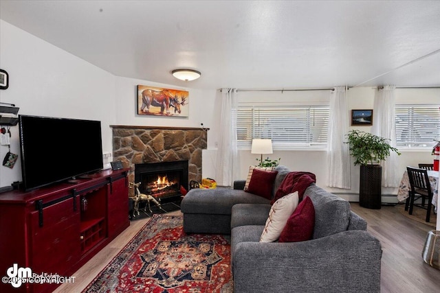 living room with a baseboard radiator, a stone fireplace, and light hardwood / wood-style floors